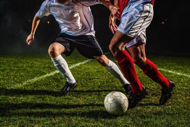 Two players contesting the ball on a floodlit grass pitch